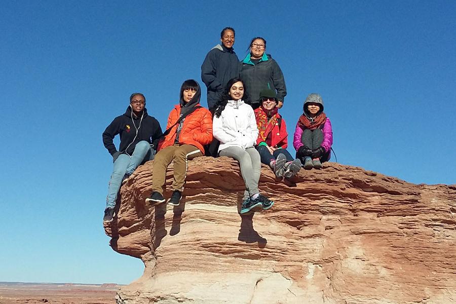 A group of students pose for a photo on a rock formation in the Navajo Nation.